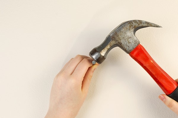 nail being hammered into white wall